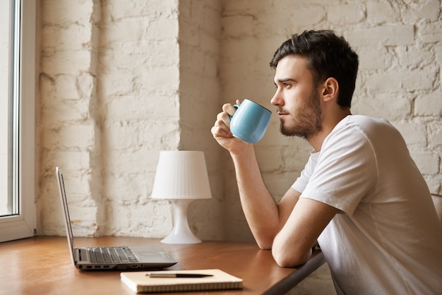 Redactor guapo con barba elegante sosteniendo una taza con café en la mano