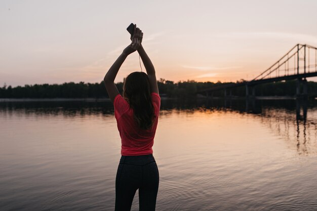 Refinada chica europea en camiseta rosa escalofriante después del entrenamiento al aire libre. retrato de mujer fascinante disfrutando de las vistas del amanecer.