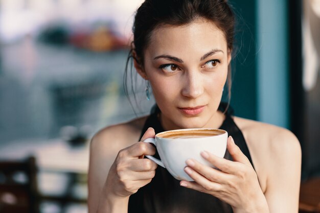 Refinada mujer disfrutando de capuchino o café con leche en un fondo vibrante y colorido en el interior.