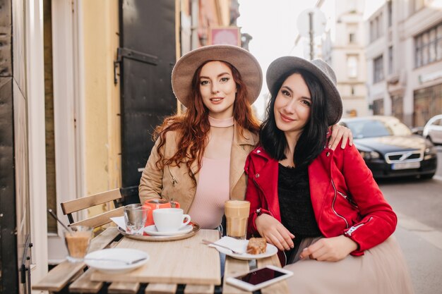 Refinada mujer pelirroja abrazando a su amiga en el café