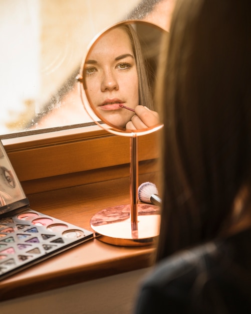 Reflejo de la cara de una modelo aplicando lápiz labial en los labios