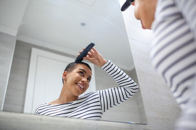 Reflejo de espejo de mujer de pelo corto en la parte superior del tanque con máquina de corte de pelo