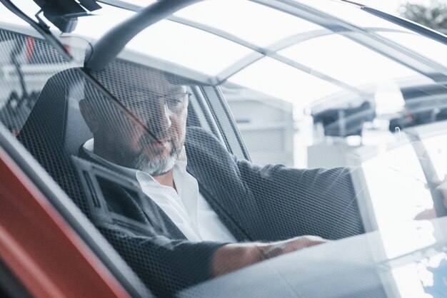 Reflejo de la habitación en la ventana delantera del coche. Senior empresario dentro