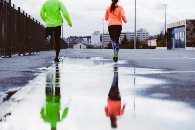 Reflexión de dos atletas corriendo en la calle en un charco