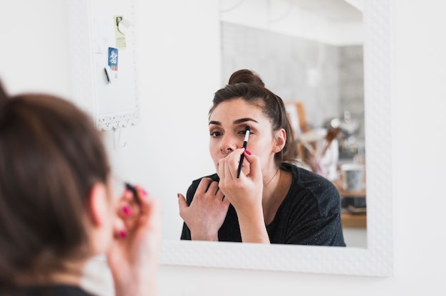 Reflexión de la mujer joven que aplica sombra de ojos con el cepillo del maquillaje