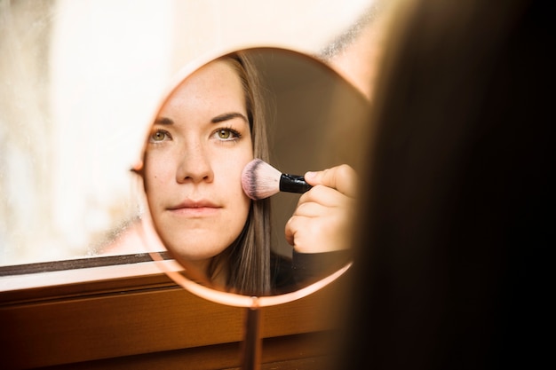 Reflexión de una mujer que aplica colorete en su cara
