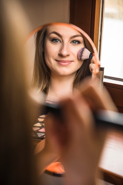 Reflexión de una mujer sonriente que aplica colorete en su cara