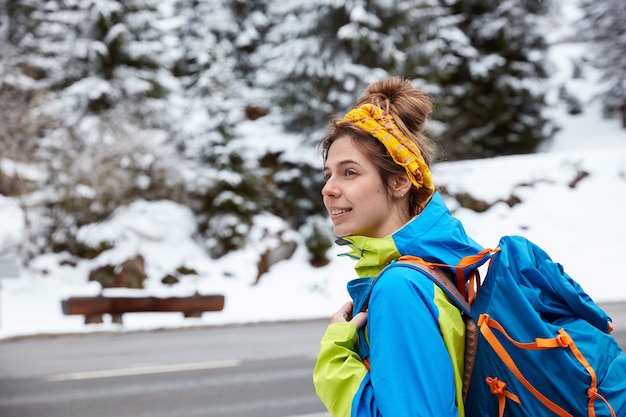 Reflexiva mujer europea centrada a un lado, paseos y caminatas cerca de montañas nevadas en invierno, disfruta del paisaje