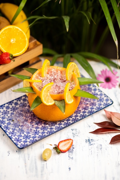 Refrescante cóctel alcohólico de verano, margarita con hielo picado y frutas cítricas dentro de naranja en un auténtico plato decorativo