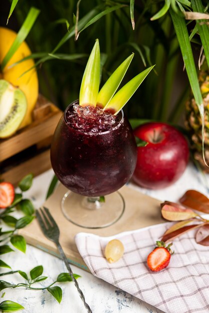 Refrescante cóctel alcohólico de verano, margarita con hielo picado y frutas cítricas dentro de un vaso con fresas y manzana en la mesa de la cocina