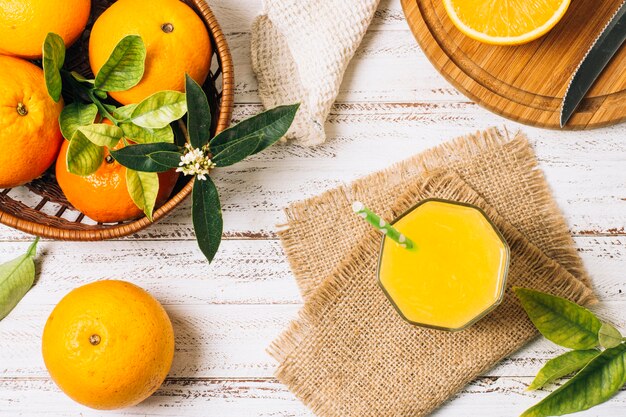 Refrescante zumo de naranja junto a cesta llena de naranjas.