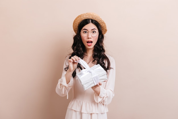 Regalo de apertura de mujer china sorprendida. Foto de estudio de mujer asiática sorprendida con regalo de cumpleaños.