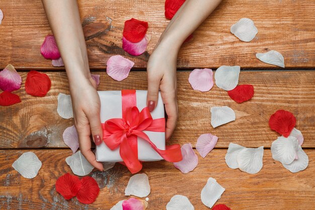 Regalo del día de San Valentín en caja blanca y manos femeninas y pétalos sobre fondo de madera