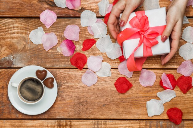 Regalo del día de San Valentín y manos femeninas en mesa de madera