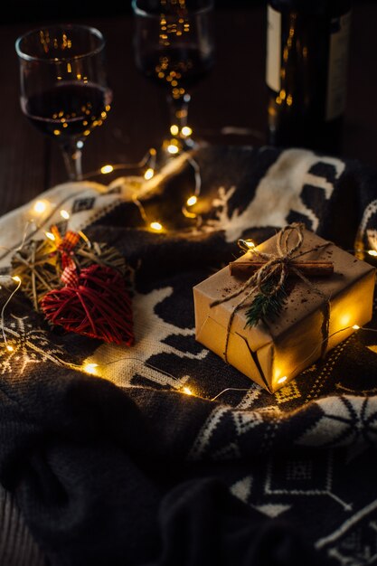 Regalo de Navidad con suéter de punto, luces de Navidad y dos copas de vino.