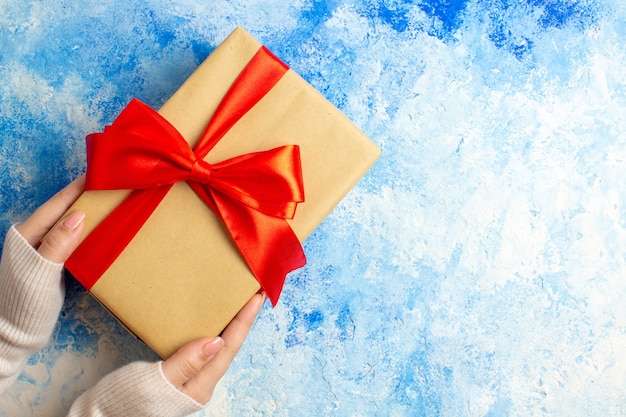 Regalo de Navidad de vista superior atado con lazo rojo en mano femenina en mesa azul con espacio libre