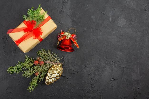 Regalo de Navidad de vista superior en papel marrón atado con colgantes de árbol de Navidad de cinta roja sobre superficie oscura