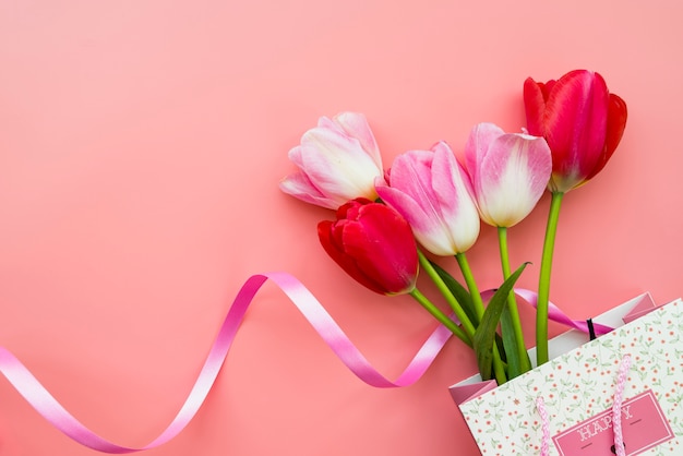 Regalo con ramo de flores en bolsa sobre fondo rosa