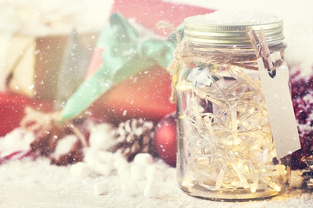 Regalo rojo con lazo verde al lado de un tarro de cristal con luces