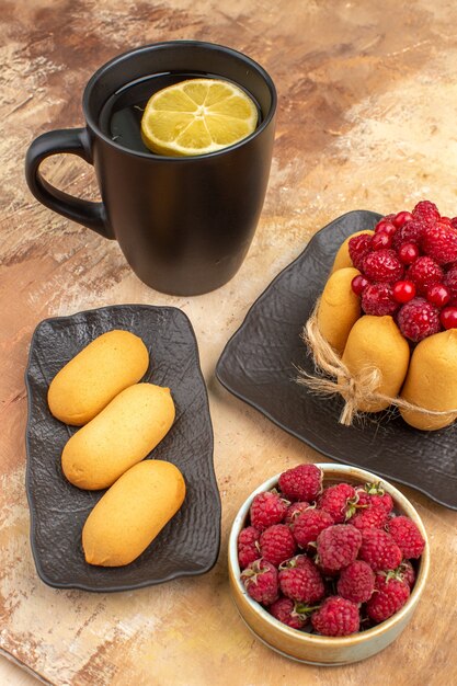 Un regalo de tarta y té en una taza negra con limón y galletas en la tabla de colores mezclados