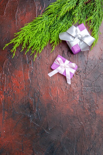 Regalos de Navidad de vista superior con caja rosa y rama de árbol de cinta blanca sobre fondo rojo oscuro