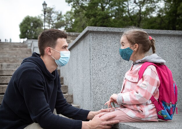 Regreso a la escuela, pandemia. Padre joven e hija pequeña en una máscara. padre cogidos de la mano con su hijo.