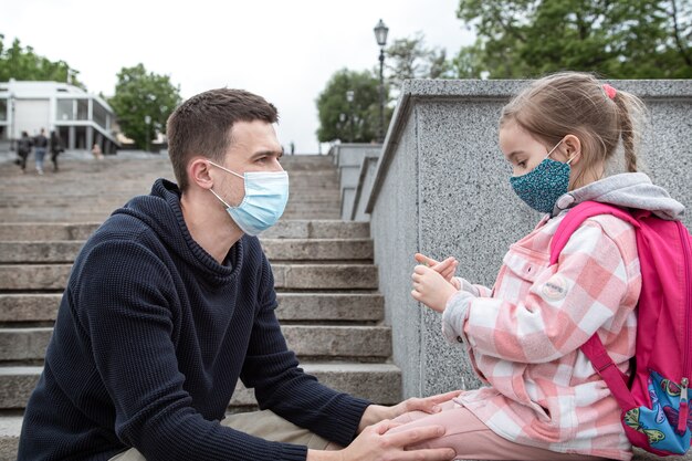 Regreso a la escuela, pandemia. Padre joven e hija pequeña en una máscara. Relaciones familiares amistosas.