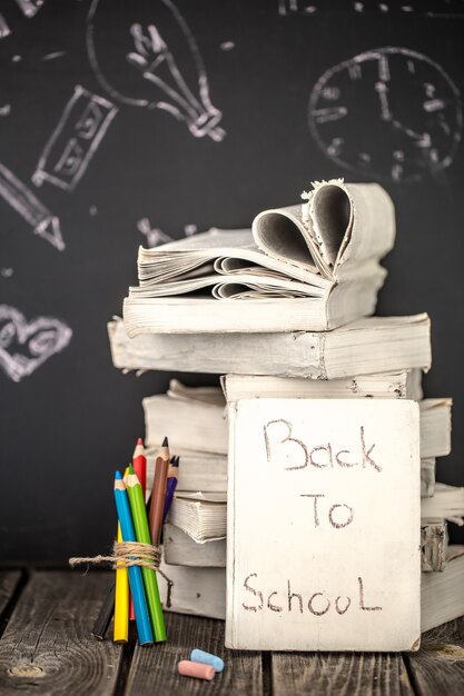 Regreso a la escuela, pila de libros y útiles escolares sobre fondo de pizarra pintado con tiza, concepto de educación