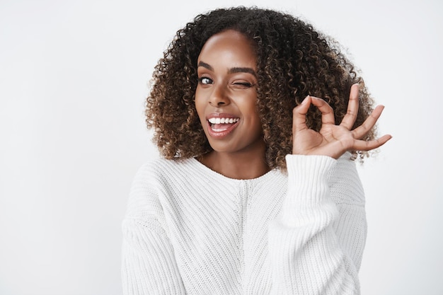 Relajada y despreocupada, segura, atractiva y exitosa mujer afroamericana guiñando un ojo descarado y sonriendo mientras muestra un gesto bien