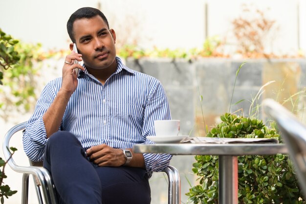 Relajado hombre hispano hablando por teléfono en el café