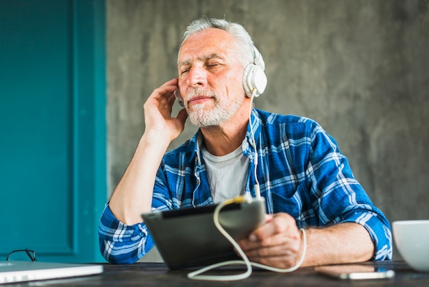 Foto gratuita relajante senior hombre escuchar música en tableta digital