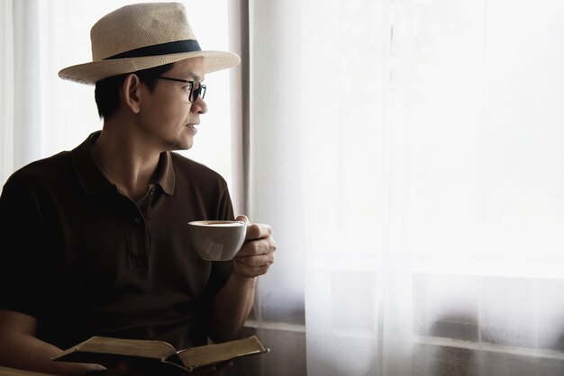 Relaje al hombre asiático que bebe un café y que lee un libro