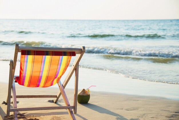 Relaje la silla de playa con coco fresco en la playa de arena limpia con mar azul y cielo despejado: el concepto de naturaleza marina