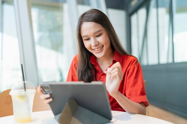 Relájese en el ocio, atractiva, inteligente, asiática, empresaria independiente, sonría y disfrute trabajando con un teléfono inteligente y una computadora portátil en un café con el concepto de ideas informales nómadas digitales de negocios de ciudad borrosa