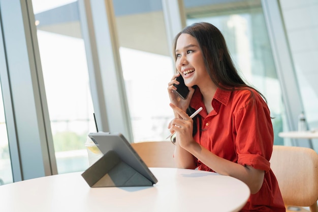 Relájese en el ocio, atractiva, inteligente, asiática, empresaria independiente, sonría y disfrute trabajando con un teléfono inteligente y una computadora portátil en un café con el concepto de ideas informales nómadas digitales de negocios de ciudad borrosa