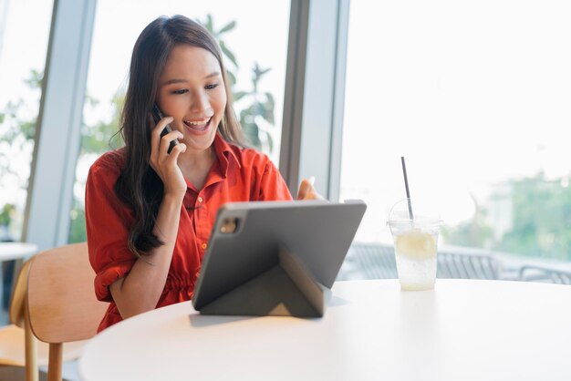 Relájese en el ocio, atractiva, inteligente, asiática, empresaria independiente, sonría y disfrute trabajando con un teléfono inteligente y una computadora portátil en un café con el concepto de ideas informales nómadas digitales de negocios de ciudad borrosa