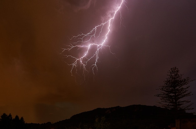 Relámpago en el cielo nocturno y montañas con árboles