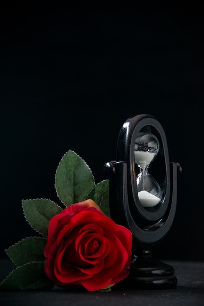 Reloj de arena negro con flor roja como memoria sobre superficie oscura
