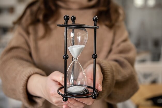 Reloj de arena vintage sobre fondo borroso de mujer, concepto de gestión del tiempo.