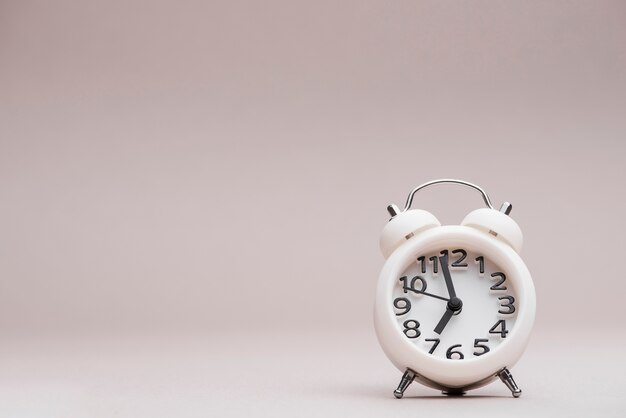 Reloj despertador miniatura blanco sobre fondo coloreado.