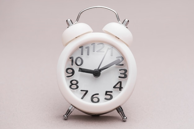 Reloj despertador miniatura blanco sobre fondo coloreado.