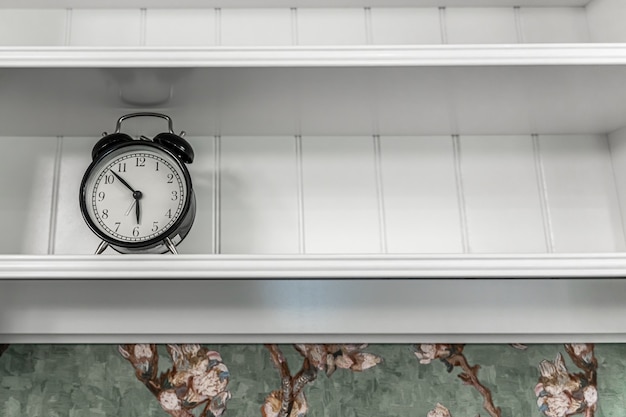 Reloj despertador vintage clásico en un estante blanco vacío en el interior de una habitación.