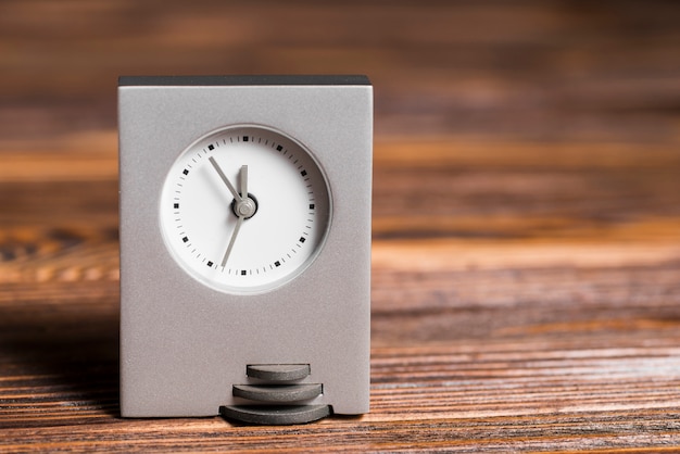 Reloj gris rectangular sobre fondo de madera con textura.