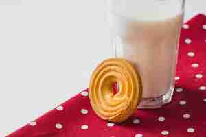 Foto gratuita remolino golpeteo galleta cerca del vaso de leche en la servilleta roja sobre el fondo blanco