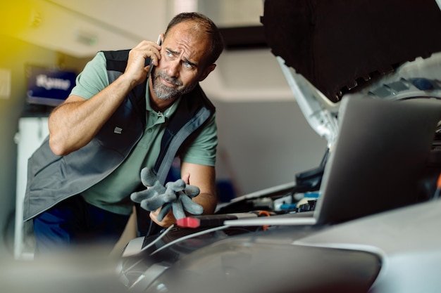 Reparación de automóviles hombre hablando por teléfono mientras trabaja en un taller