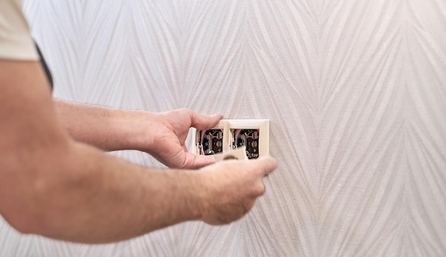 Reparación eléctrica e instalación de enchufe e interruptor de toma de corriente Un hombre caucásico electricista instala una toma de corriente con alicates durante una reparación Manos del maestro primer plano durante el trabajo