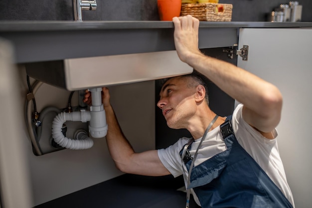Reparación de fontanero Un hombre de mediana edad atento y experimentado que examina el fondo del fregadero de la cocina