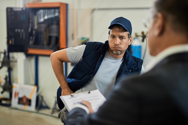 Foto gratuita reparador de automóviles angustiado hablando con su gerente sobre informes problemáticos en un taller