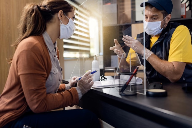 Reparador de automóviles comunicándose con un cliente mientras usa mascarilla protectora y guantes en la oficina