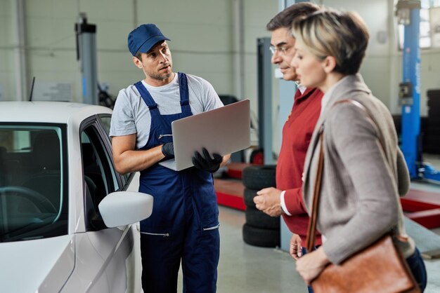 Reparador de automóviles comunicándose con sus clientes mientras usa una computadora portátil en un taller